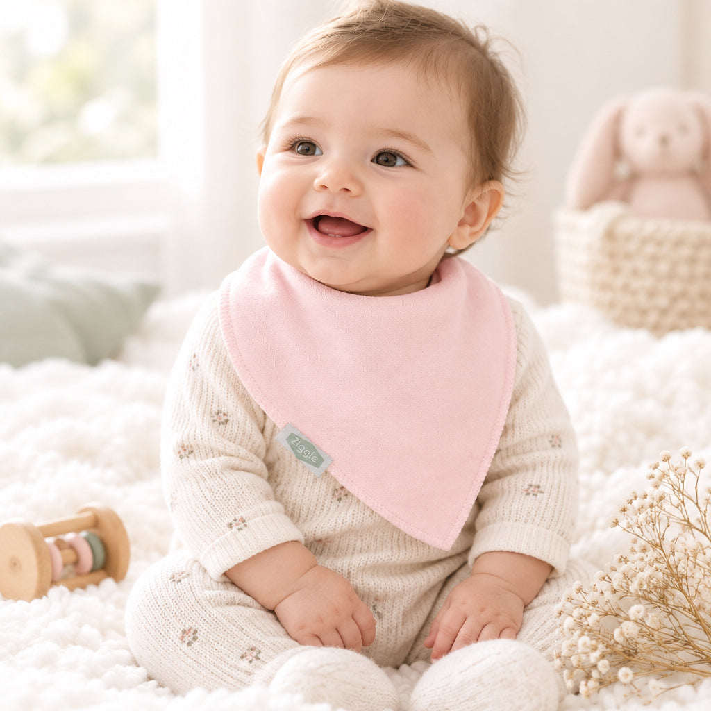 Baby wearing a plain pale pink pointed bandana bib over a patterned top