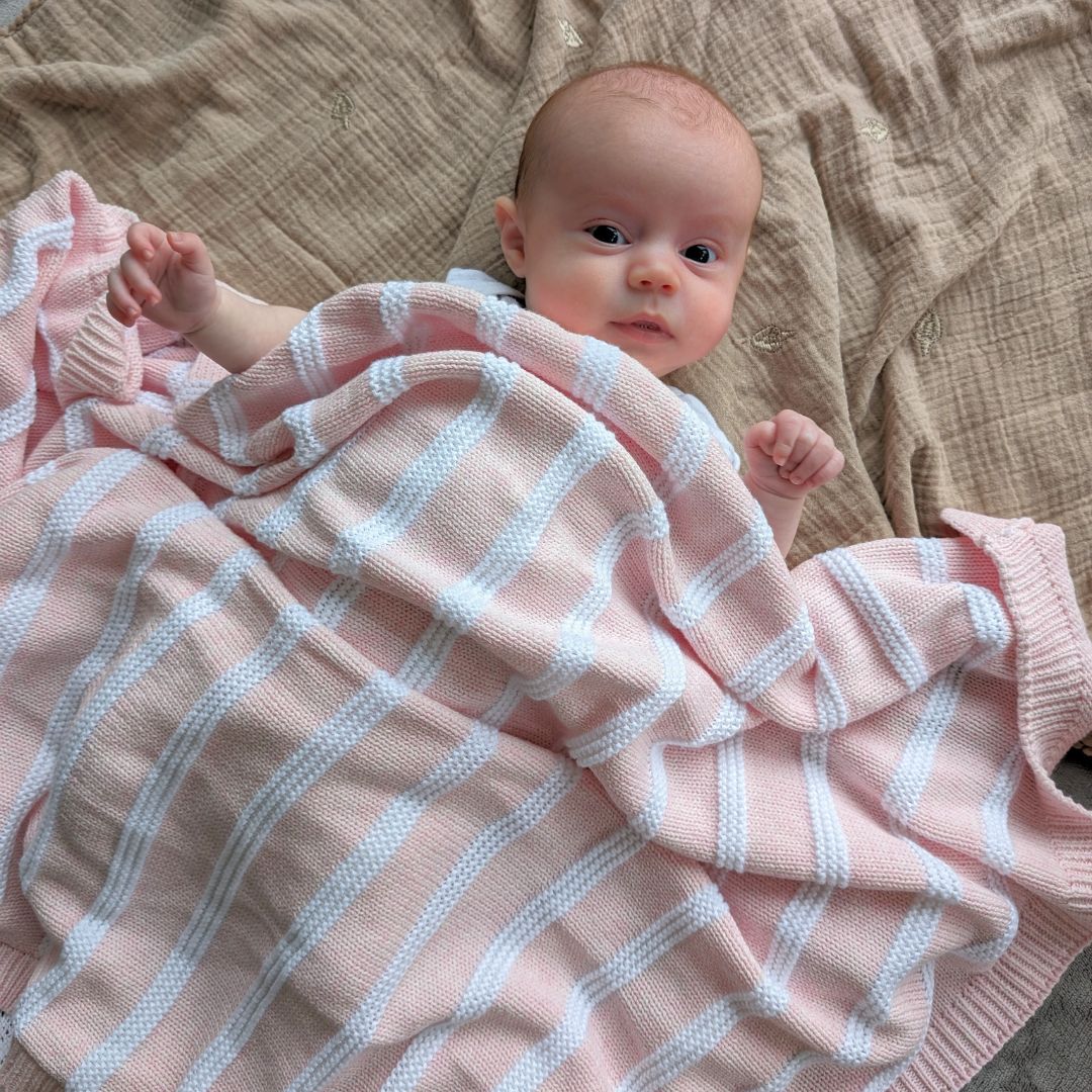 Baby blanket with pink and white stripes covering a baby