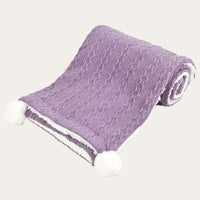 Purple cable knit baby blanket with pom poms a the corners in a light purple lilac colour