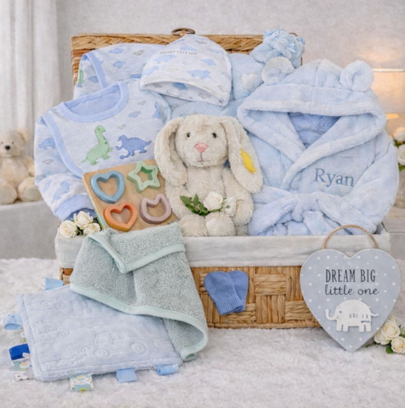 Baby boy gift basket with dinosaur clothing and blue hooded dressing gown in a hamper.