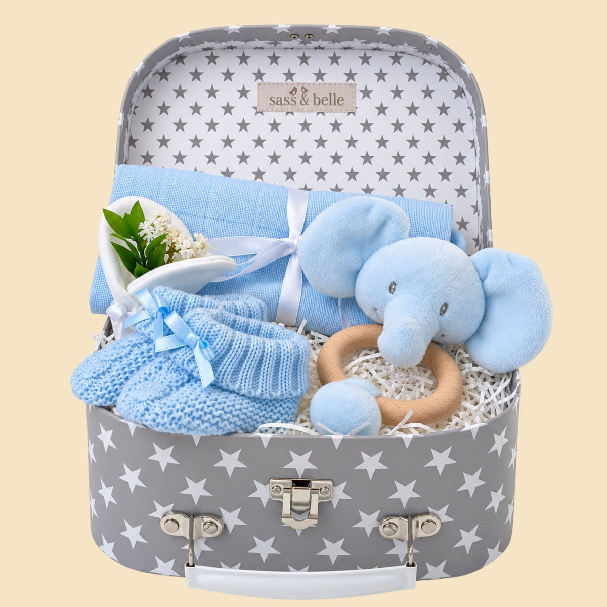 Baby boy gifts hamper with blue elephant toy, knitted booties, and other items in a luggage trunk.