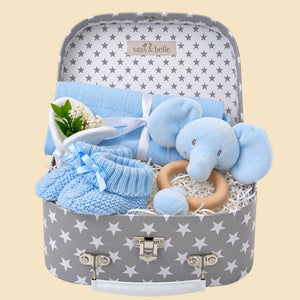 Baby boy gifts hamper with blue elephant toy, knitted booties, and other items in a luggage trunk.