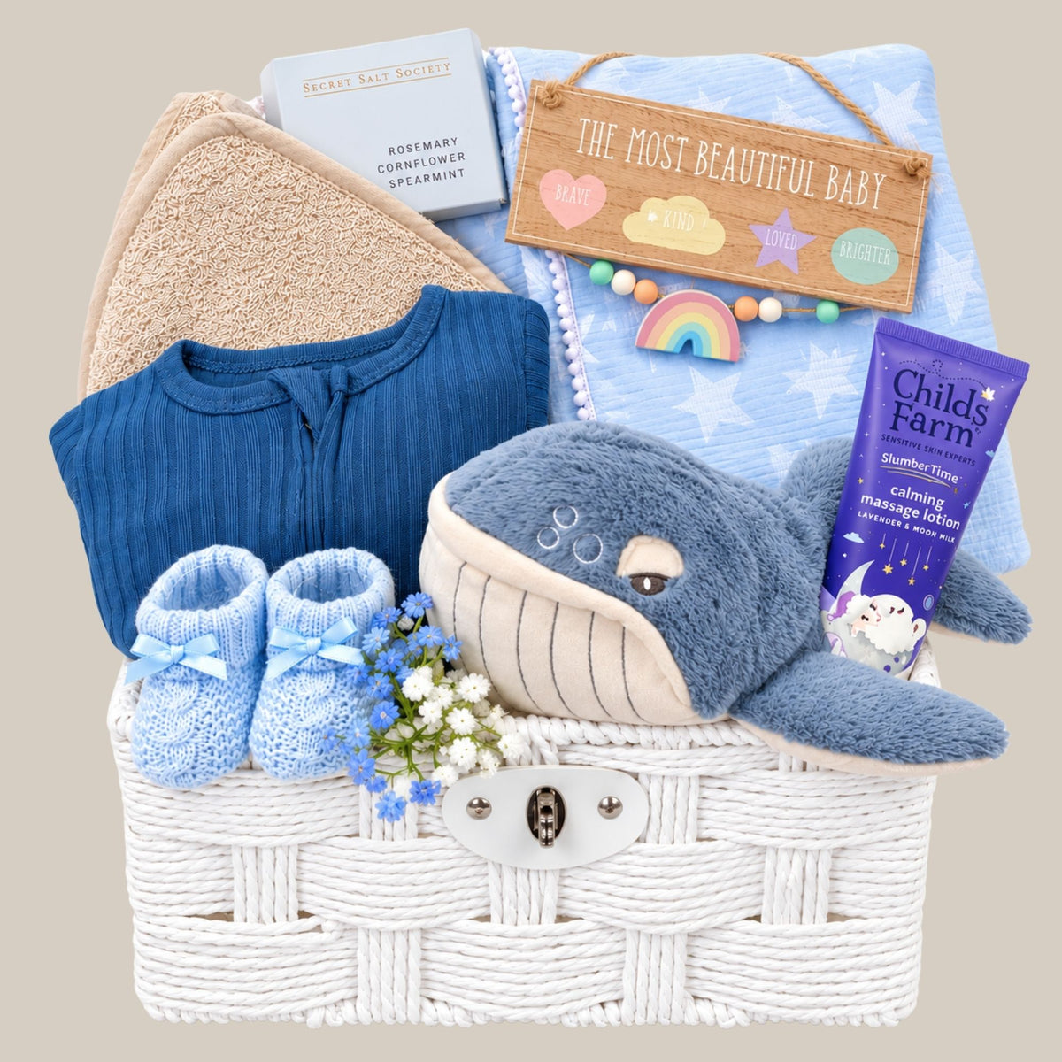 Baby boy hamper basket with gifts including blue newborn clothing set, plush whale soft toy and blanket.