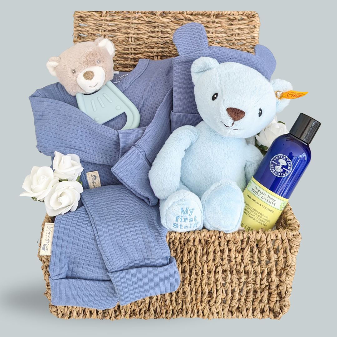 baby boy hamper basket with gifts including blue steiff teddy bear, teething toy, baby lotion and organic clothing set.