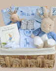 Baby boy hamper with gifts including blue blanket and Peter Rabbit baby comforter next to a white hamper basket.