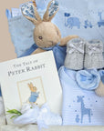 Baby boy hamper with gifts including blue blanket and Peter Rabbit baby comforter next to a white hamper basket.