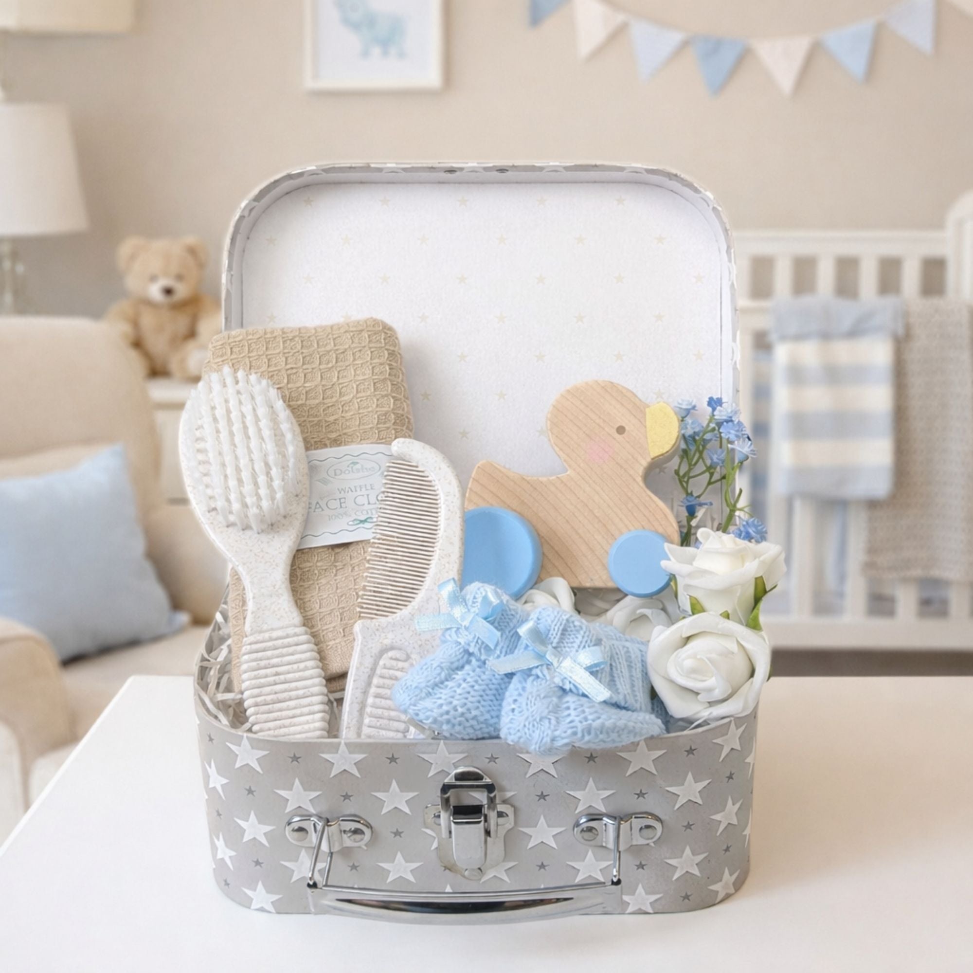 Newborn baby boy gifts in a hamper trunk with wooden duck and blue baby booties.