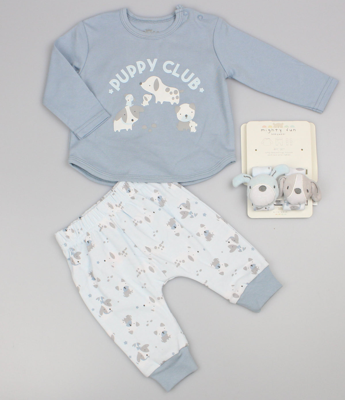 Baby boy clothes laid flat on grey: blue Puppy Club top, white printed trousers and matching wrist rattles.