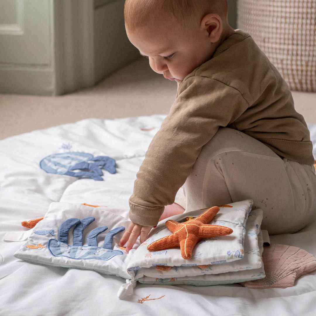 Baby touching the open Coastline fabric book and its raised starfish.