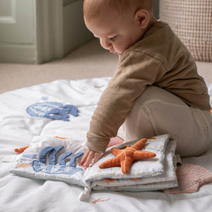 Baby touching the open Coastline fabric book and its raised starfish.