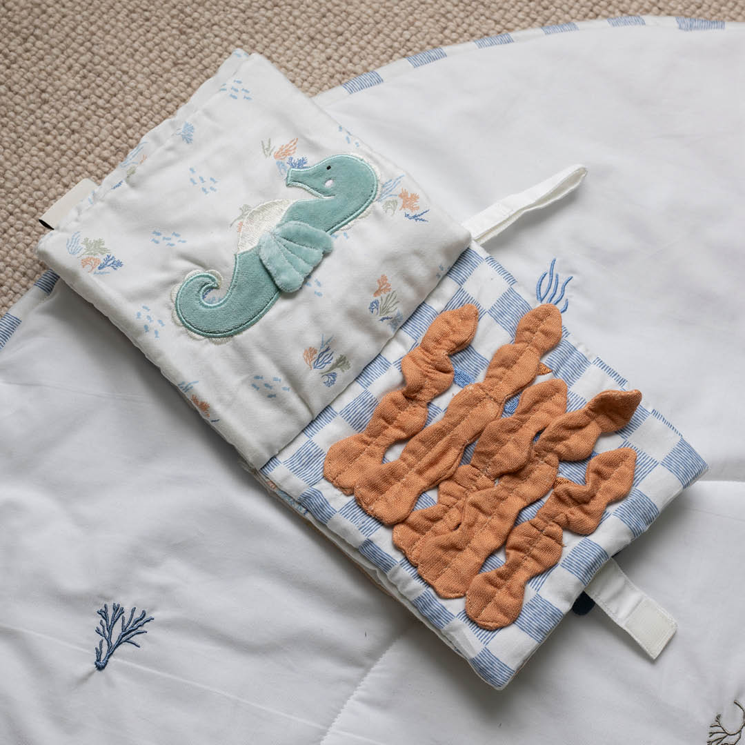 Open fabric book showing a green seahorse and textured orange seaweed.