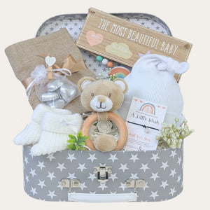 A new baby gift hamper set in a keepsake luggage trunk, including a white knot hat, knitted booties