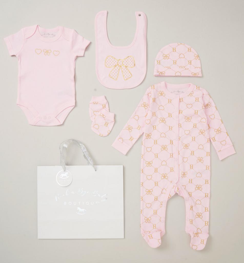 A 5 piece baby girl clothes set in pale poink with a heart & bow pattern. Includes bodysuit, bobygrow, hat, mittens and bib.