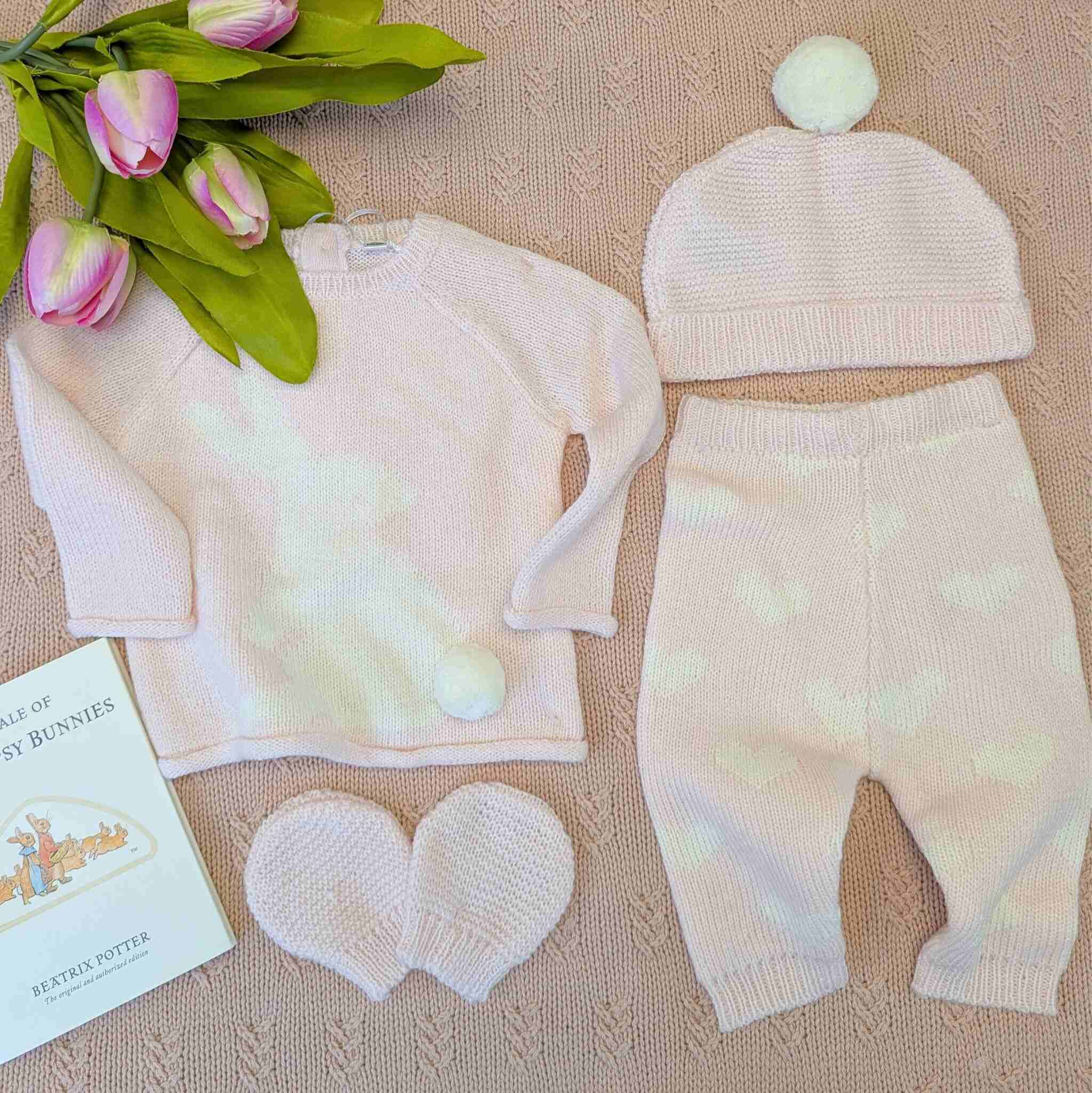 Pink baby girl outfit set with jumper, trousers, hat and mittens. With a white bunny and hearts pattern