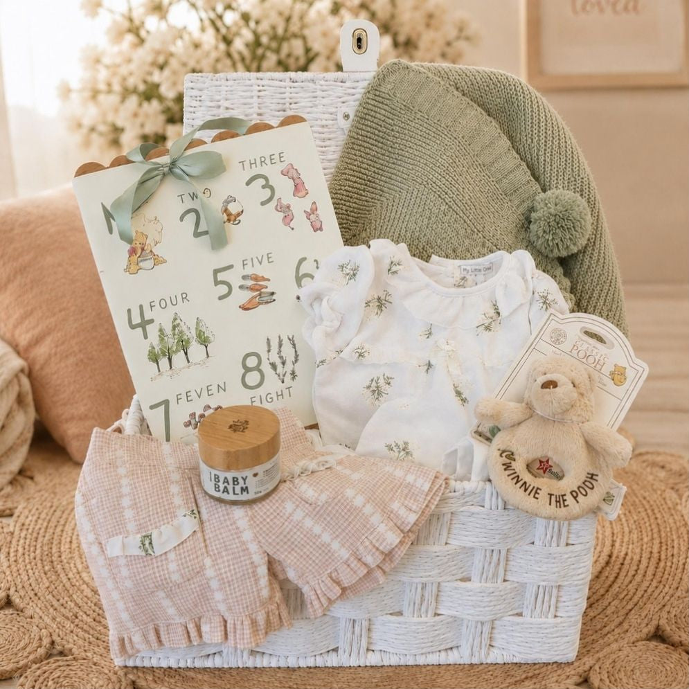 Baby girl hamper basket with gifts including baby blanket, clothing set and winnie the pooh toy packed in a white hamper