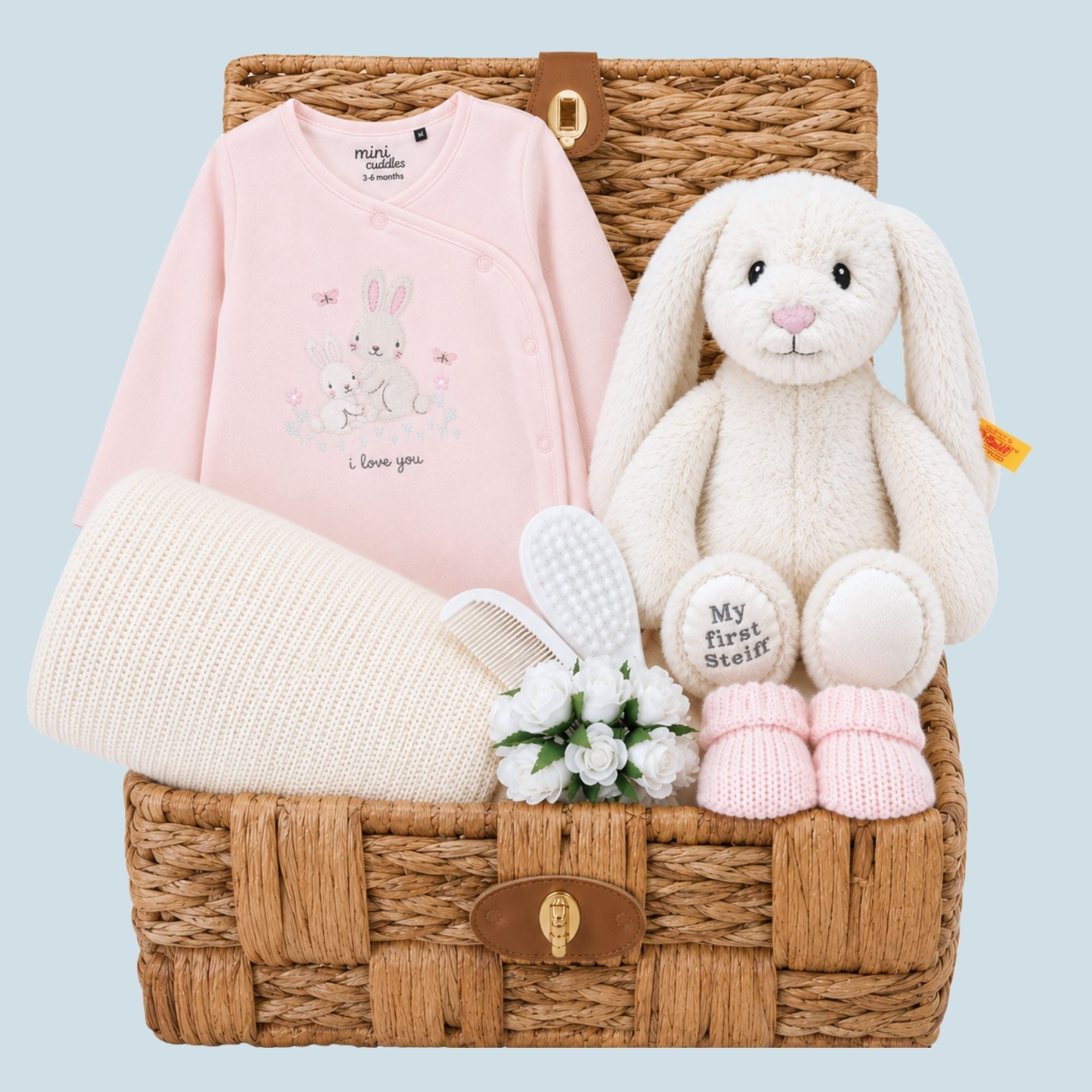 Baby girl gifts hamper with presents including steiff bunny toy, blanket and booties in a woven basket.