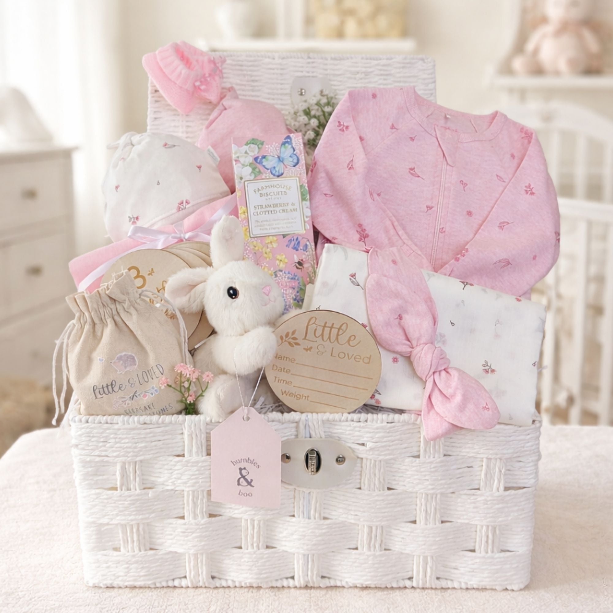 Newborn baby girl gifts in a white hamper basket with organic pink baby clothing and bunny soft toy.