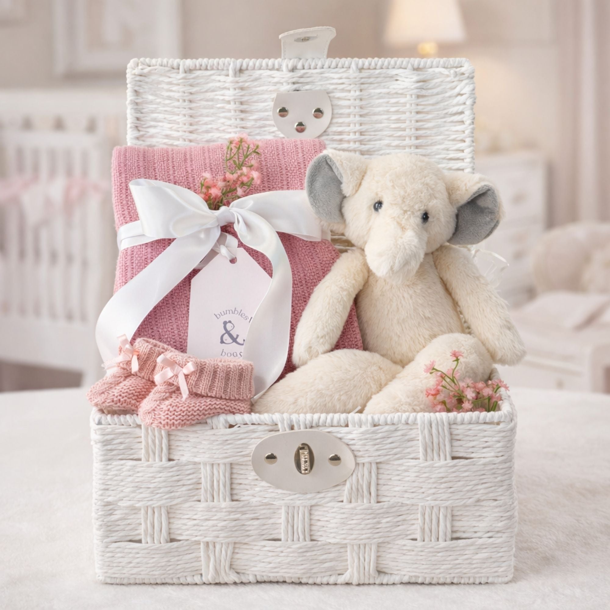 Baby girl gifts in a white hamper basket with an elephant and blossom pink cellular blanket.