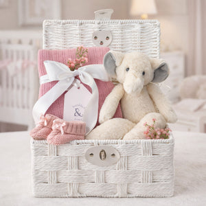 Baby girl gifts in a white hamper basket with an elephant and blossom pink cellular blanket.