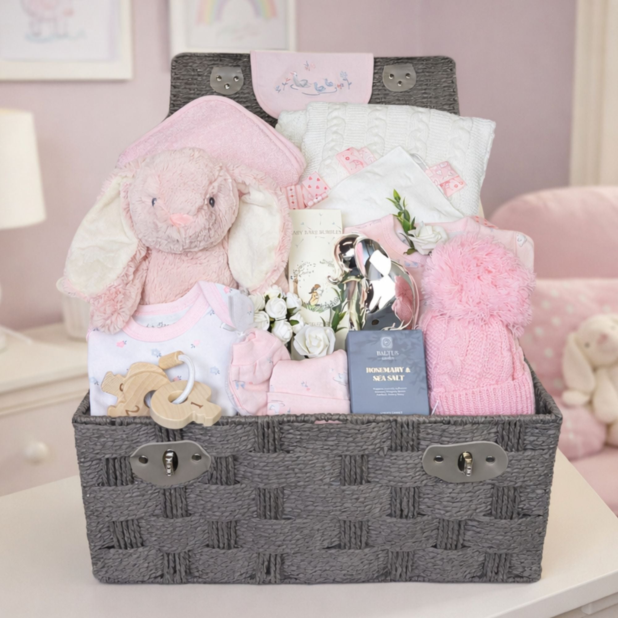 Presents for a baby girl in a hamper basket. Gifts include bunny and blanket and silver money box.
