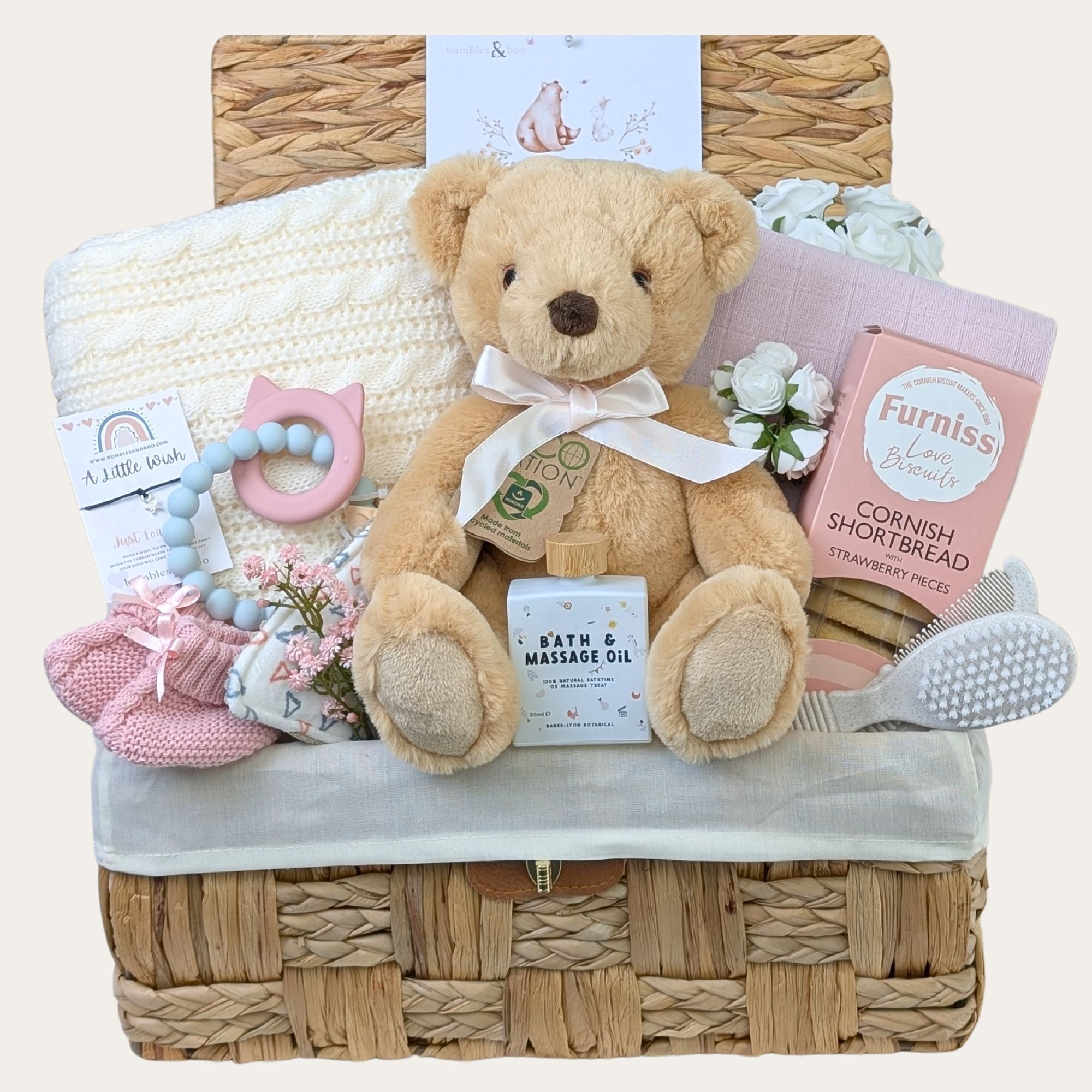 Baby girl hamper with gifts including teddy and blanket in soft pink and cream tones.