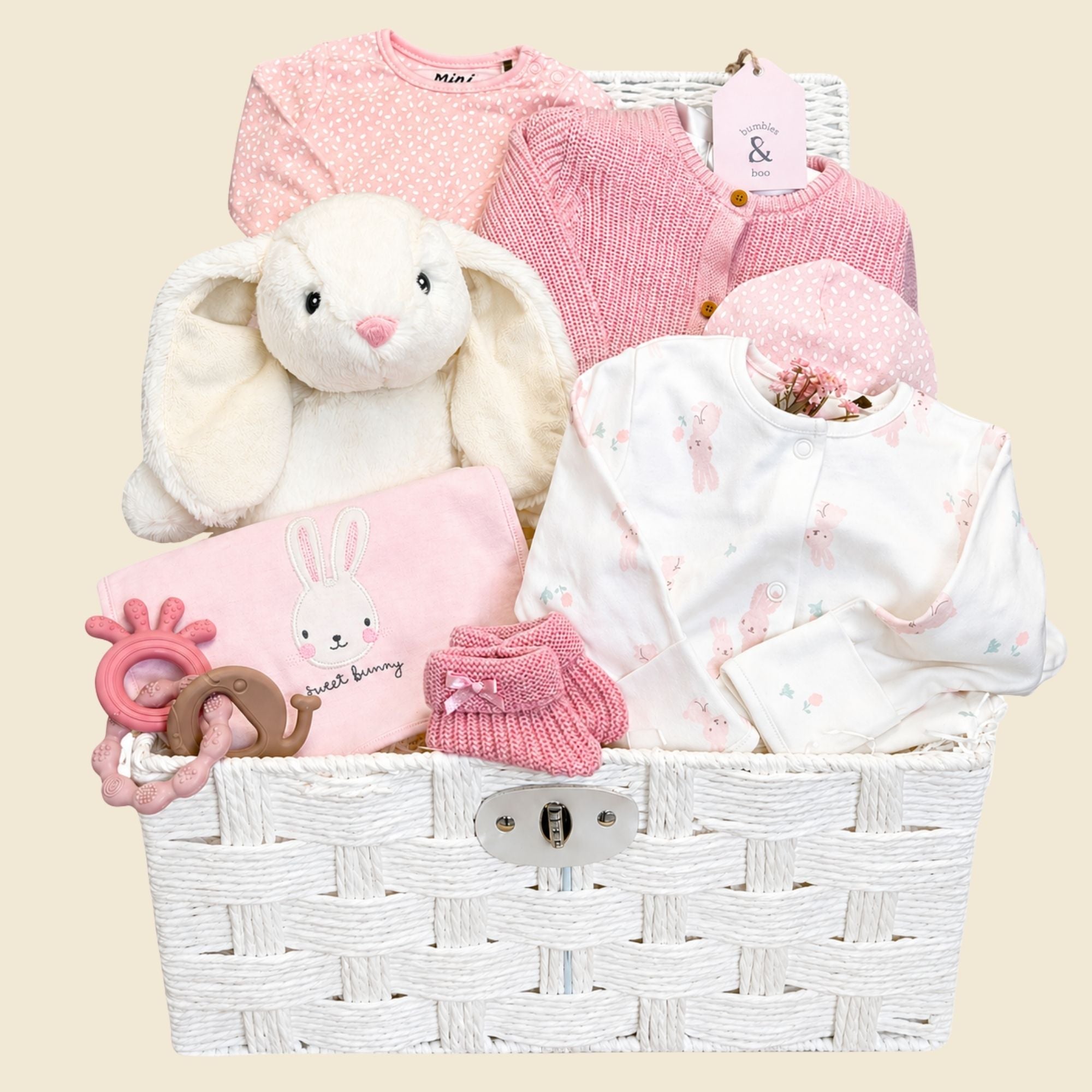 Luxury baby girl hamper basket with gifts including white and pink bunny-themed baby clothes and white rabbit soft toy. 