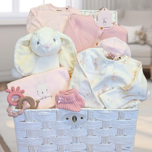 Luxury baby girl hamper basket with gifts includung white and pink bunny-themed baby clothes and white rabbit soft toy. 