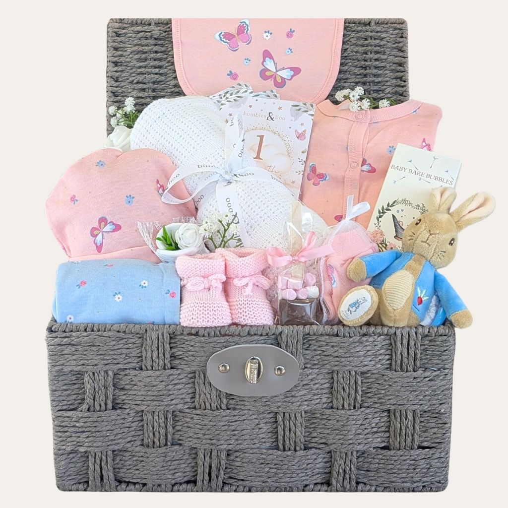 Baby girl hamper with gifts including pink newborn clothing set, and peter rabbit soft toy in a basket by Bumbles and Boo