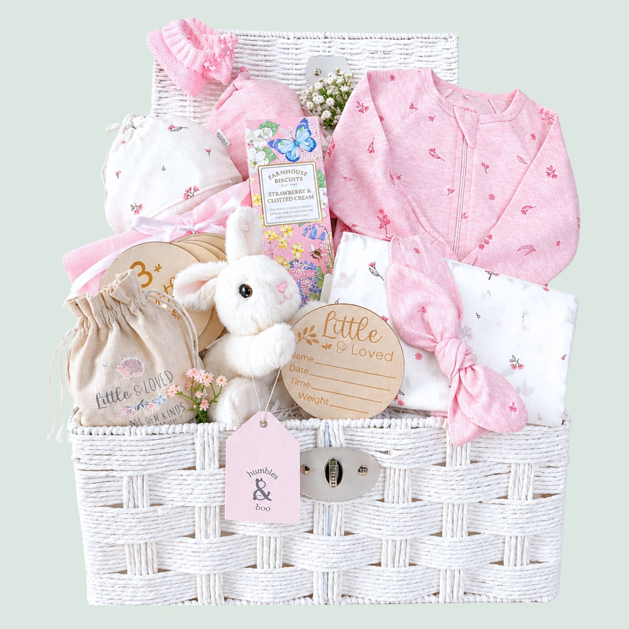 Newborn baby girl gifts in a white hamper basket with organic pink baby clothing and bunny soft toy.