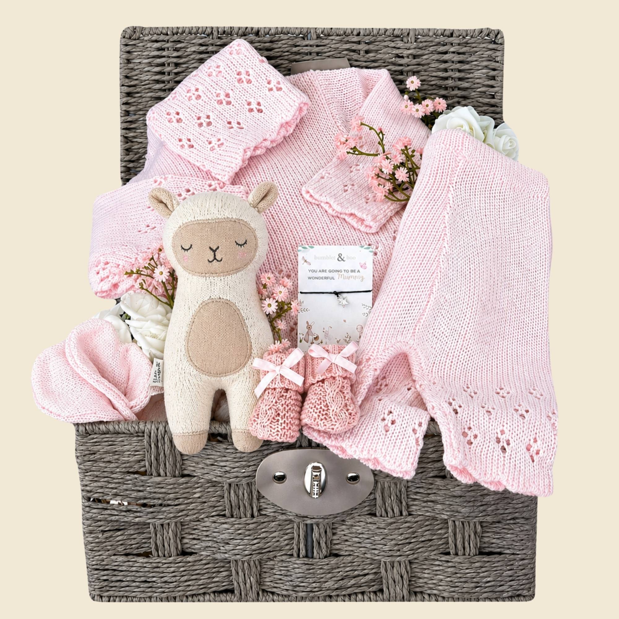 Baby girl hamper basket packed with gifts to welcome a new baby girl with pink knit clothing and a cuddly lamb.