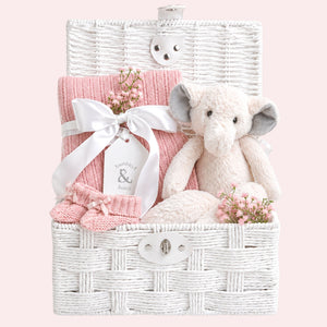 Baby girl gifts in a white hamper basket with an elephant and blossom pink cellular blanket.