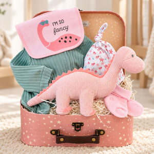 A baby girl gift set arranged inside a pink suitcase with star print. The set includes a pink dinosaur plush toy, a teal ribbed long-sleeve sleepsuit and a pink and white heart-patterned hat and bib set