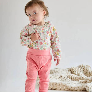 Child wearing a floral top and pink pants on a plain background