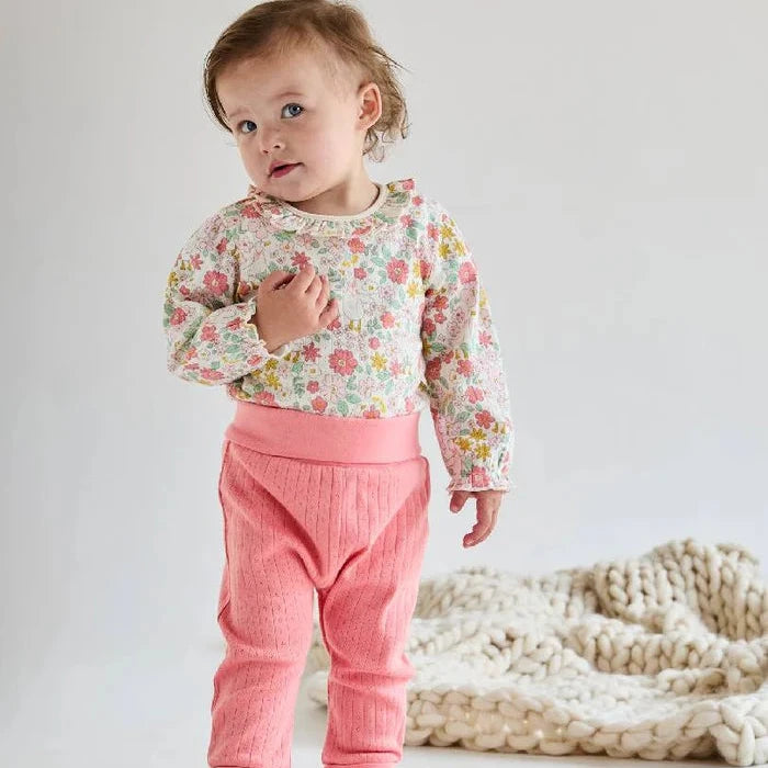 Child wearing a floral top and pink pants on a plain background