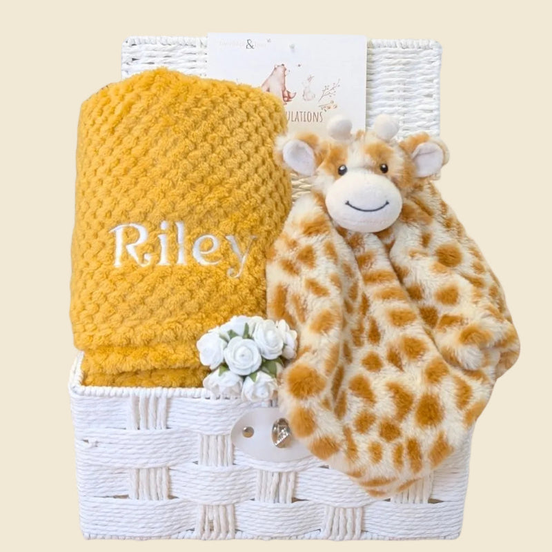 Baby hamper basket packed with gifts including soft giraffe comforter and yellow blanket personalised with the name Riley