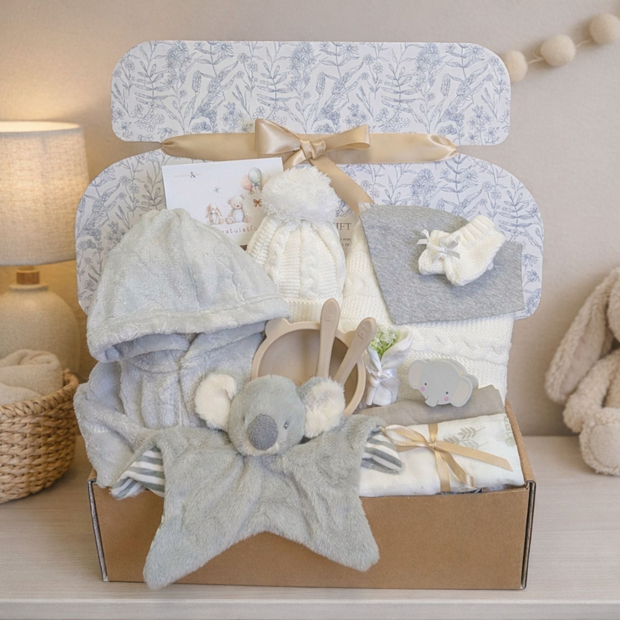 Baby hamper gift box packed with presents for a new baby. Includes a koala soft toy comforter and white baby blanket