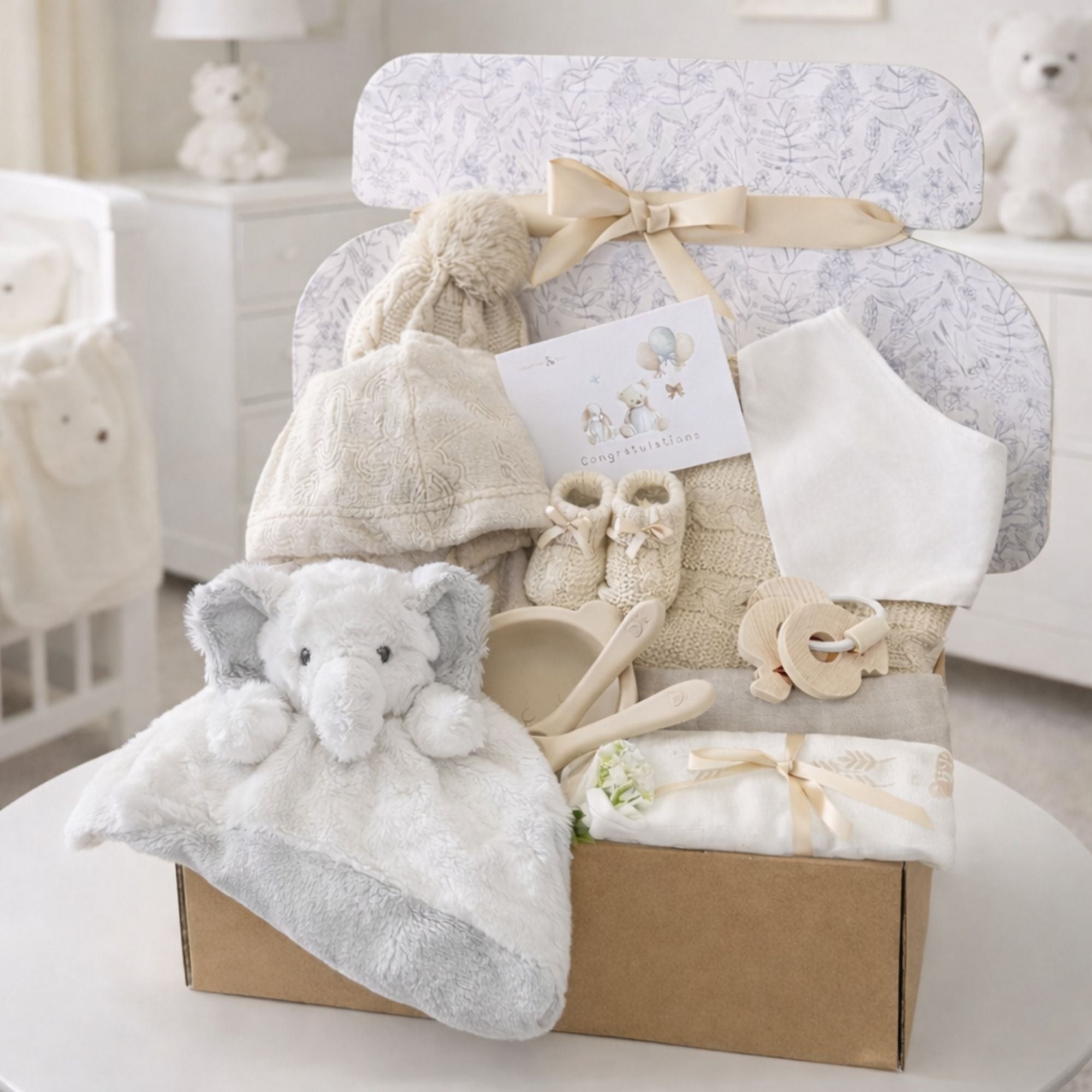 Newborn baby hamper gift box with presents including beige blanket and bath robe and elephant comforter.