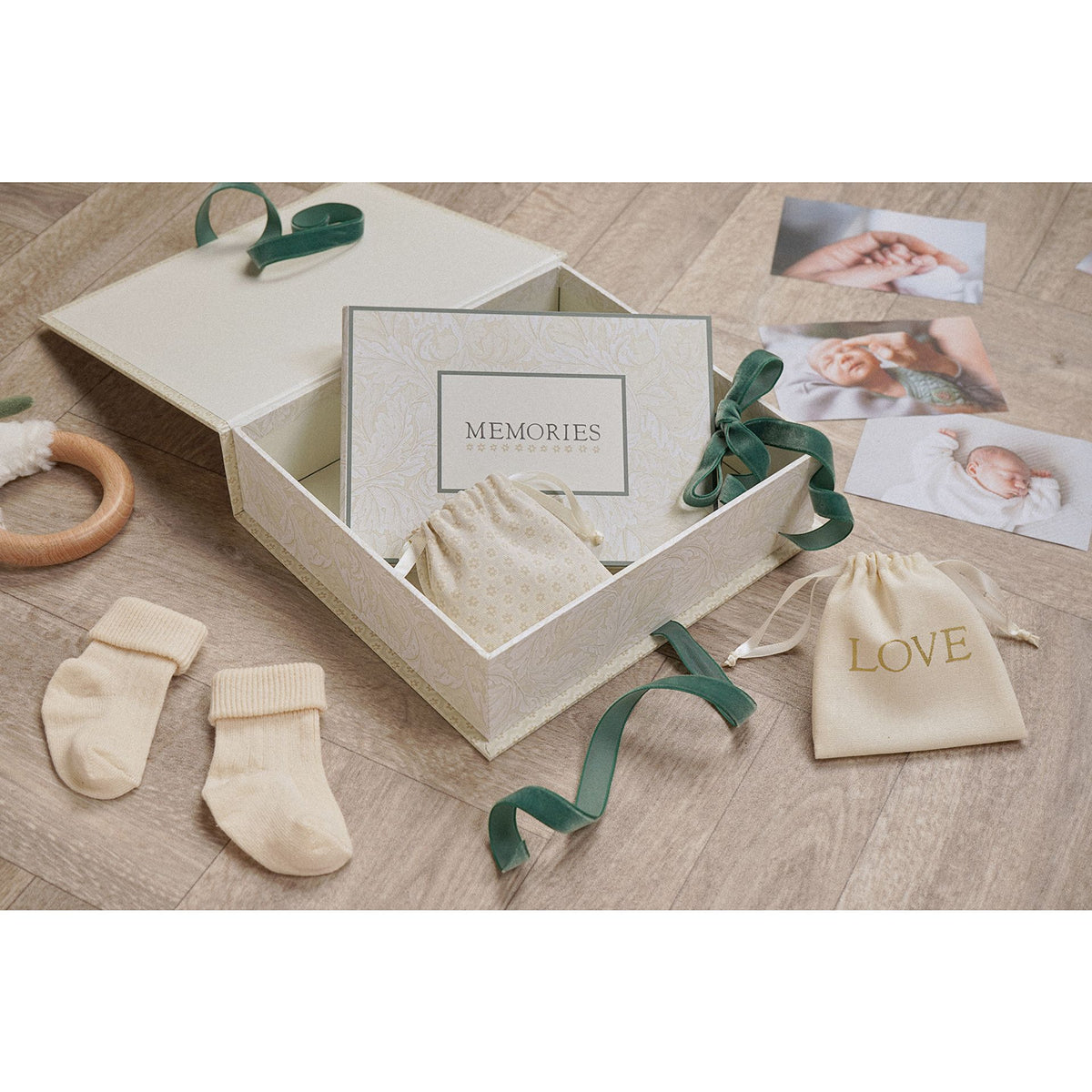 Open neutral baby keepsake box with pouches and a ‘MEMORIES’ item, styled beside photographs and socks.