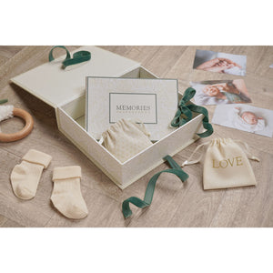 Open neutral baby keepsake box with pouches and a ‘MEMORIES’ item, styled beside photographs and socks.