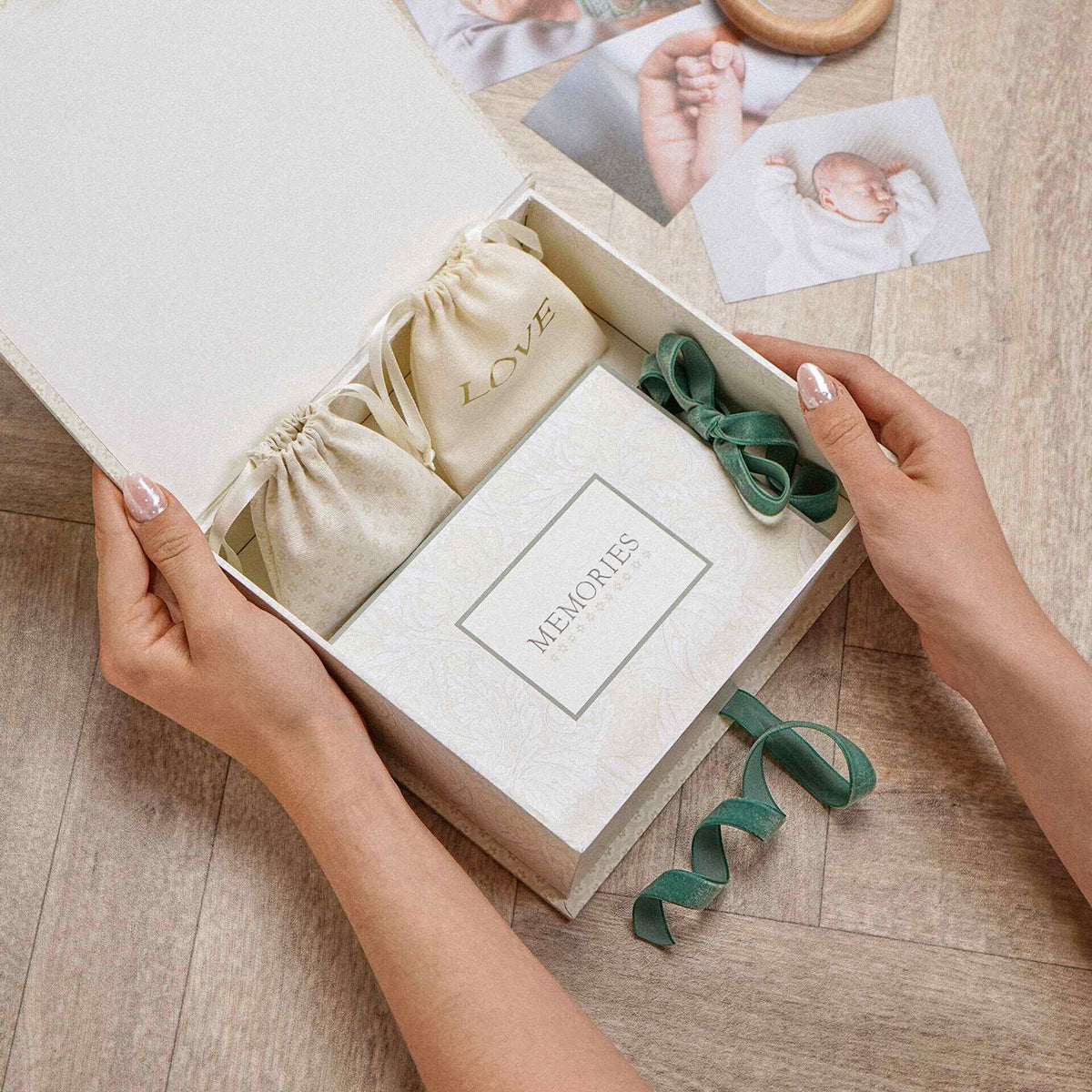 Hands holding an open baby keepsake box containing drawstring pouches and a ribbon-tied ‘MEMORIES’ item.