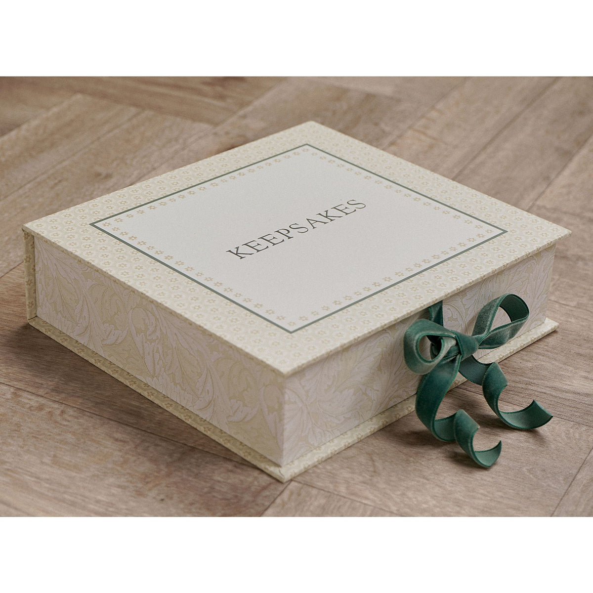 Closed cream patterned keepsake box with ‘KEEPSAKES’ on the lid and green ribbon ties.