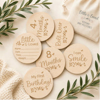 A set of round wooden baby milestone markers with engraved text and floral designs