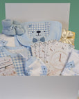 baby shower gifts in a white box with blue clothes with a teddy on the bib and milestone cards.
