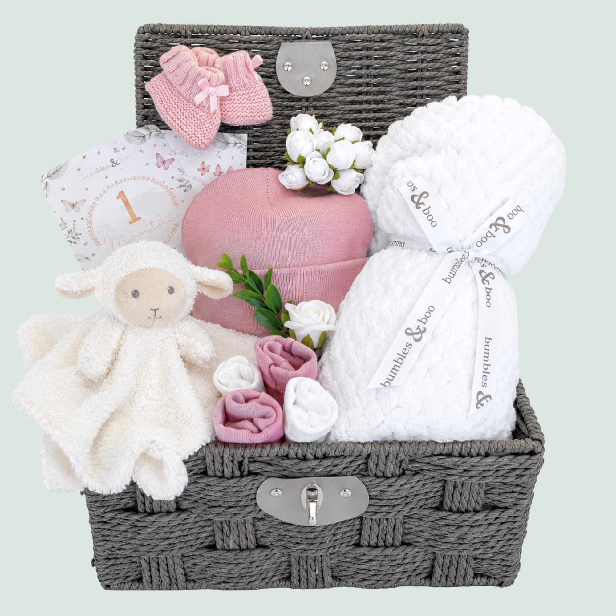 Baby shower gifts basket with pink baby clothes, lamb soft toy and white blanket packed in a wicker hamper by Bumbles & Boo.