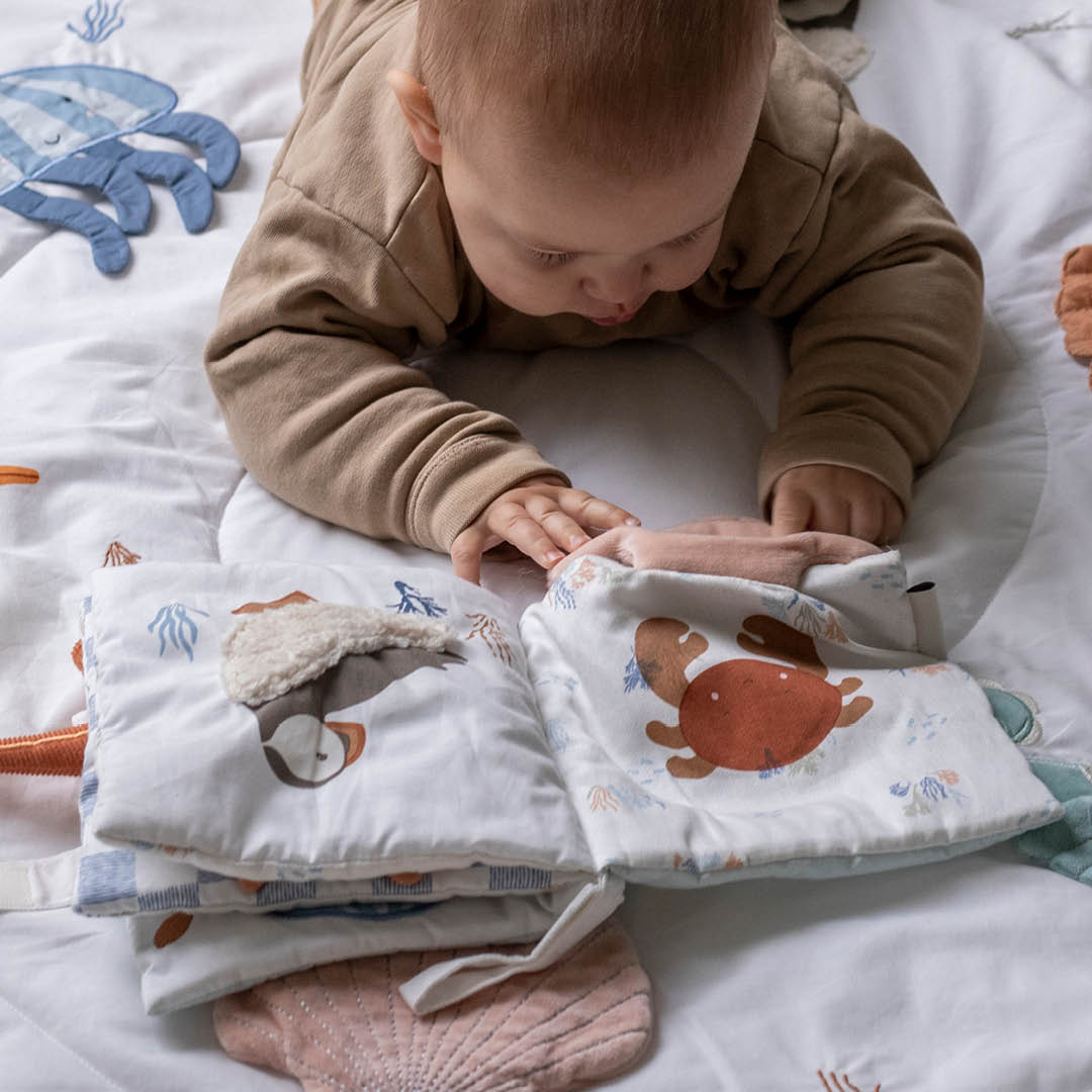 Baby turning a page of the seaside fabric book with a puffin illustration.