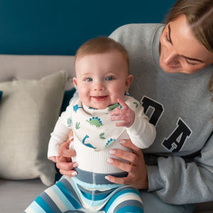 Baby wearing dinosaur print dribble bib with white outfit