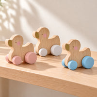 Three available wooden duck designs with pink, white and blue wheels displayed upright on a pale oak playroom shelf.