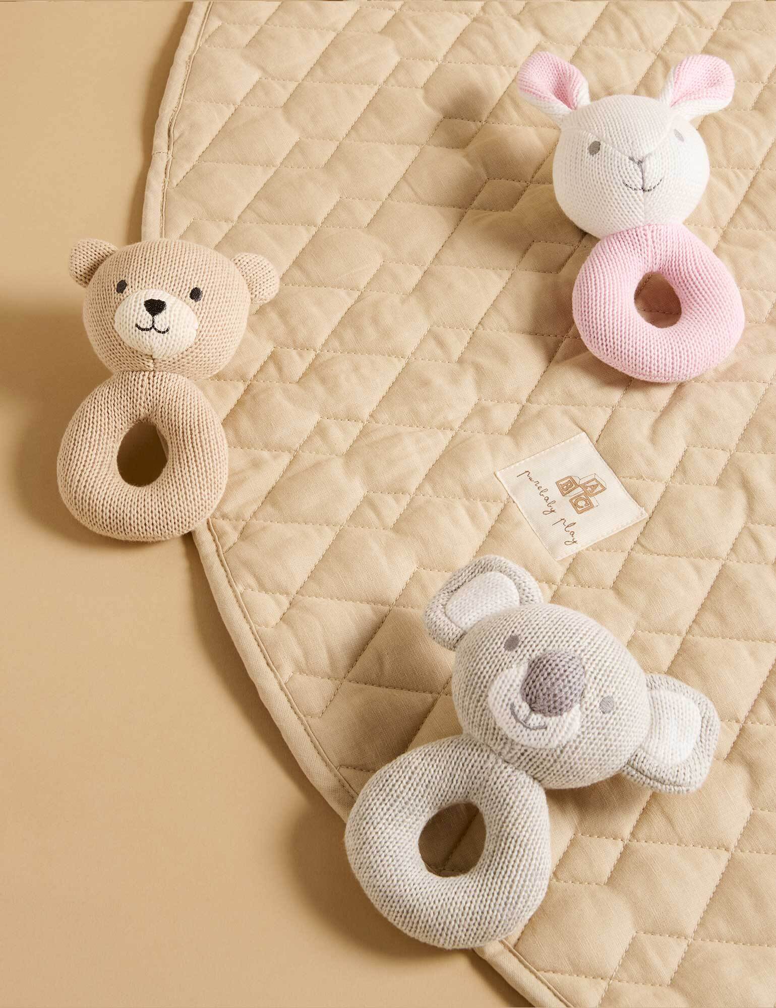 Baby toys including a bear and a pink animal on a quilted blanket.