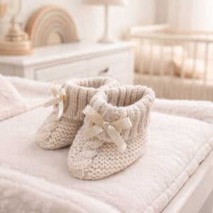 Beige knit baby booties with a little bow and turnover tops