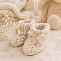 Beige knit baby booties with a little bow and turnover tops